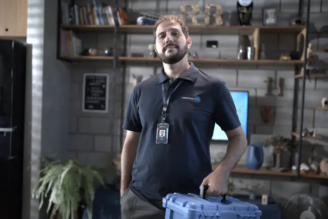 Técnico da Fibercom de uniforme e crachá, segurando uma maleta de ferramentas azul.